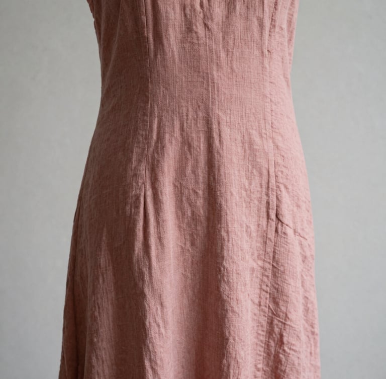 Close-up of a draped dusty rose linen dress on a minimalist mannequin, soft side lighting highlighting fabric texture