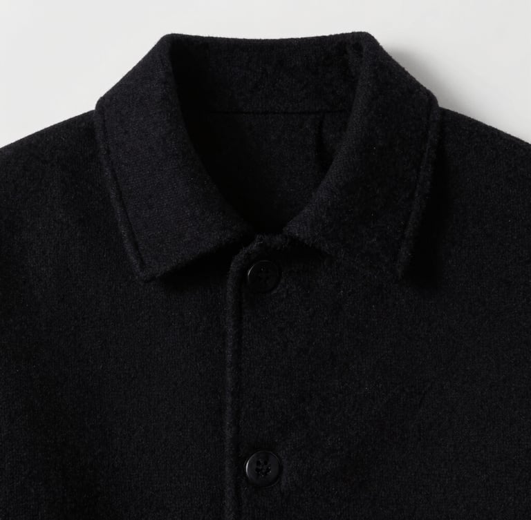 Detail shot of structural seams on a heavy black wool collar, sharp directional studio lighting, high contrast, desaturated cool tones
