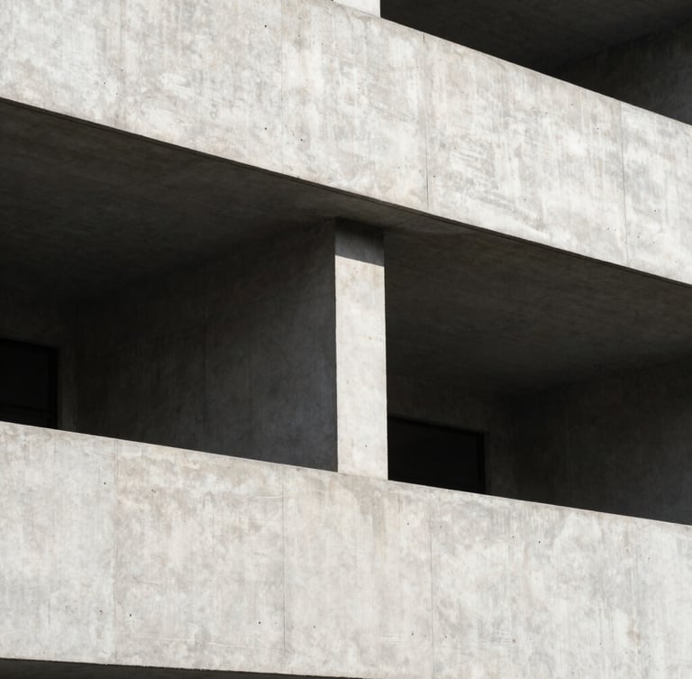 A high-contrast, minimalist architectural photograph of a concrete building facade under bright daylight, clean geometric lines and deep shadows creating structured negative space.