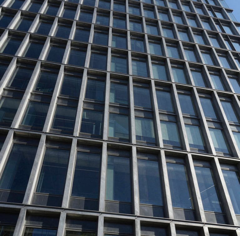 Low-angle architectural photograph of a completed glass and steel building facade, sharp shadows, high-contrast daylight, emphasizing structural joints and clean lines, wide-angle perspective.