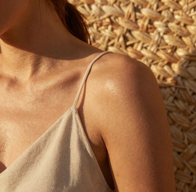 Close-up of sun-kissed skin and raw linen fabric, golden hour light filtering through woven straw, warm organic textures.