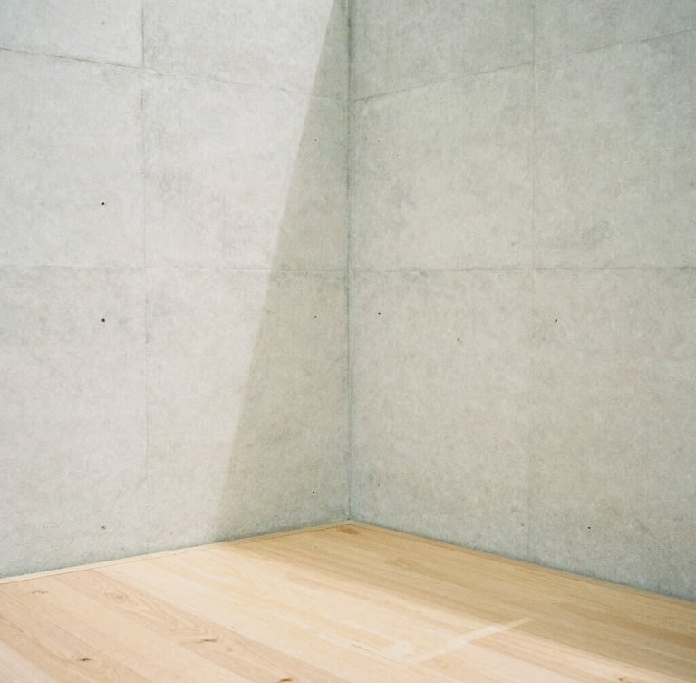 A minimalist concrete wall corner meeting a light oak floor, soft diffused overcast daylight casting subtle shadows, quiet architectural composition, medium format film look.