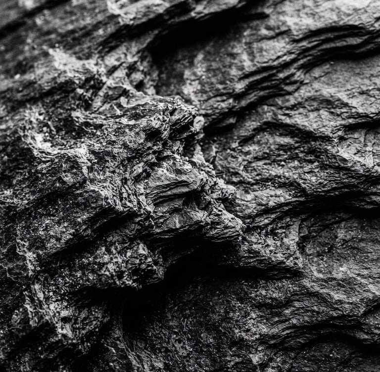Macro photography of dark slate texture with deep shadows, dramatic side-lighting, high-contrast black and white, tactile organic material, 35mm