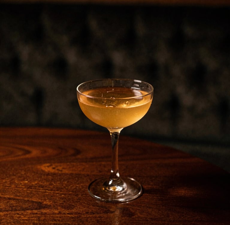 Close-up of a perfectly crafted cocktail in a premium glass, resting on a dark wood table with a blurred velvet texture in the background, dramatic chiaroscuro lighting, warm amber tones, shallow depth of field, 35mm film.