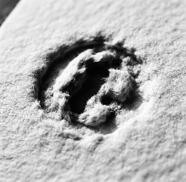 Macro close-up of heavy paper stock with deep letterpress indentation, stark shadows, high contrast black and white photography, 35mm film grain