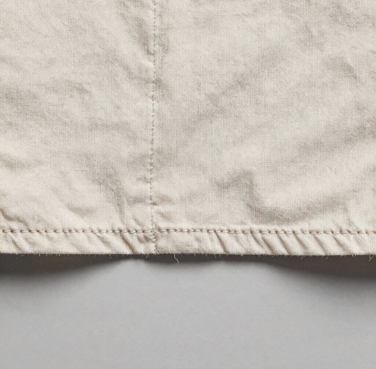 Extreme macro photograph of a single-stitch hem on a heavily faded vintage cotton shirt, showing individual thread fibers, flat studio lighting, neutral grey background