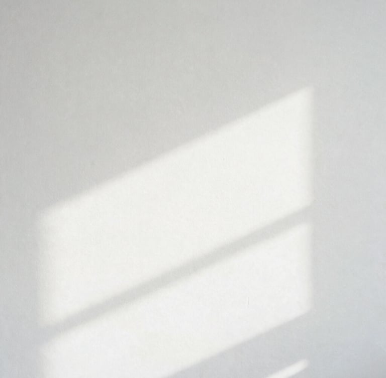 Minimalist high-key photography of soft diffuse white light casting pale architectural shadows on a clean plaster wall, 35mm