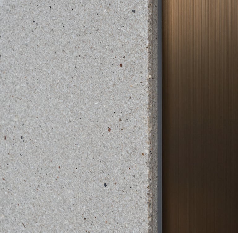 Macro portrait texture of raw split-face travertine stone meeting a brushed bronze profile, sharp architectural shadow, overcast daylight.