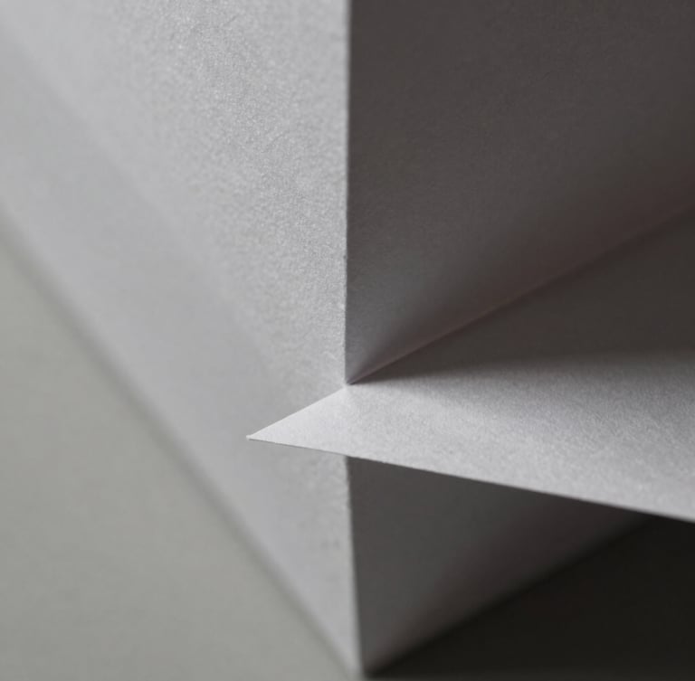 Macro close-up of sharp geometric paper folds, hard directional side-light, crisp paper textures, sharp shadows, neutral monochrome tones, 50mm.