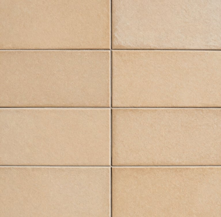 Close-up architectural photograph of perfectly aligned large-format ceramic tiles on a wall, sharp grout lines, warm sand tones, natural side lighting highlighting the flat surface, 35mm.