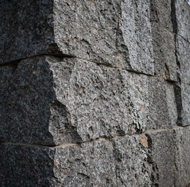 A vertical portrait of a massive hand-chiseled granite foundation wall, deep mortar joints catching dramatic side lighting, overcast natural daylight, raw stone textures.