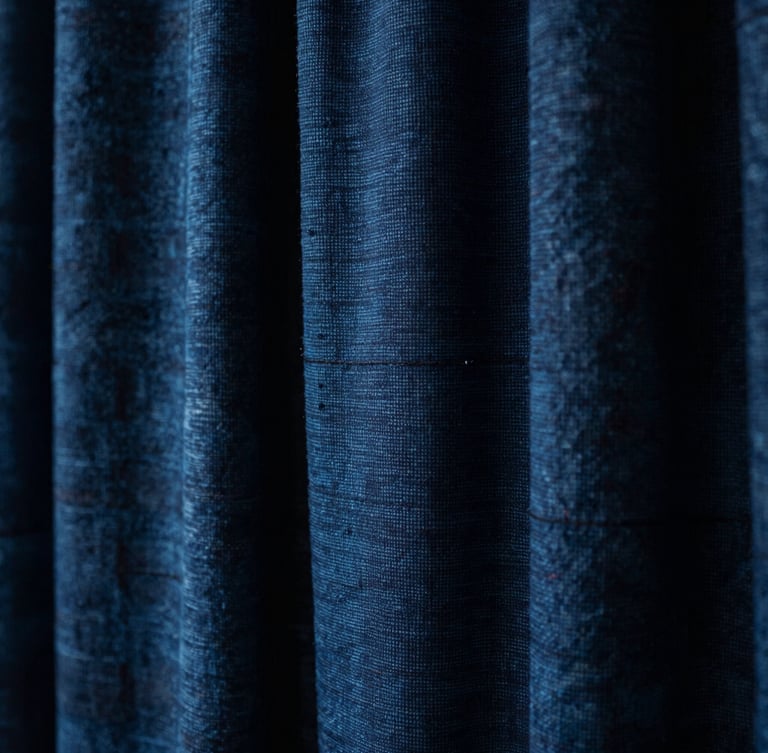 Tight macro shot of hand-loomed indigo textiles showing rich mineral-dyed grain and heavy weave, dramatic low-key window lighting.
