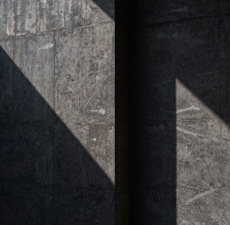 Abstract close-up of a monolithic dark concrete wall with sharp brutalist shadows, cast in low-key side-lighting, solid and secure.