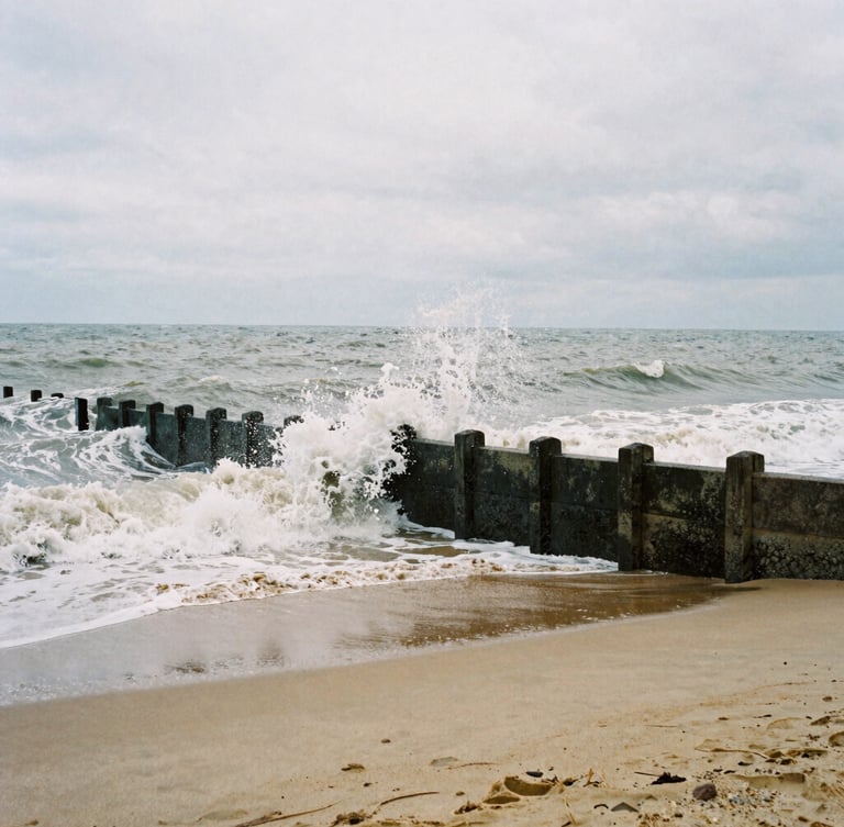 Moody film photography of the overcast Margate coastline, raw sea-navy waves crashing against concrete sea walls, desaturated sand tones, high contrast, 35mm