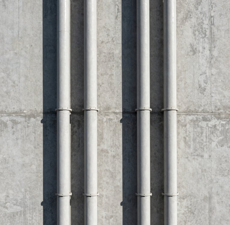 Symmetrical vertical conduit runs along a textured concrete wall, clean industrial shadows, straight-on architectural framing.
