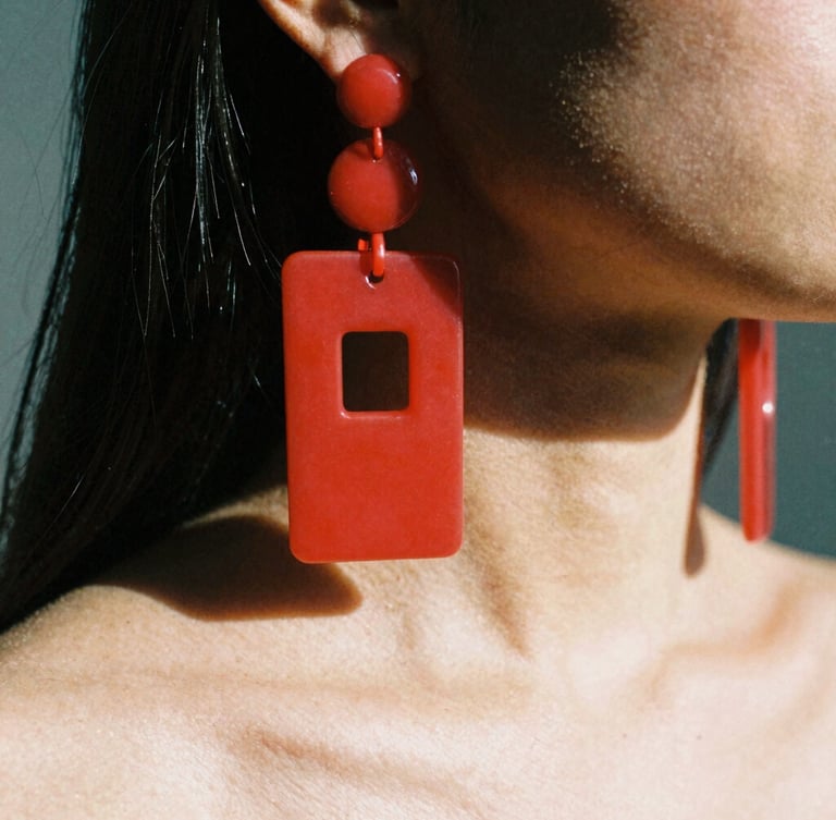 Extreme macro shot of heavy red acrylic earrings hanging to the shoulder of a model, high-contrast direct sunlight, sharp dark shadows, avant-garde fashion photography, 35mm film.