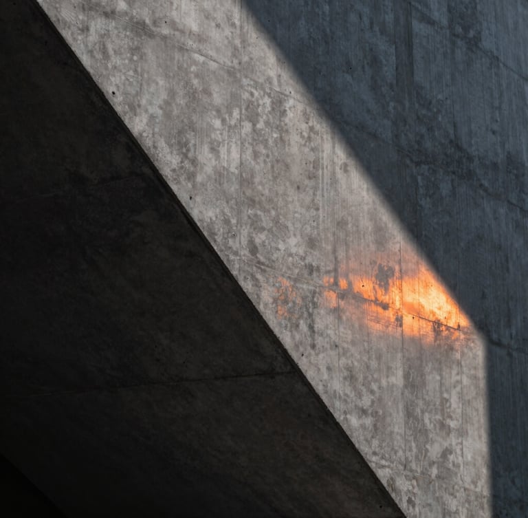 Close-up of a high-end dark architectural concrete wall with sharp linear shadows and a single orange light strip reflecting on the surface, clean minimal composition