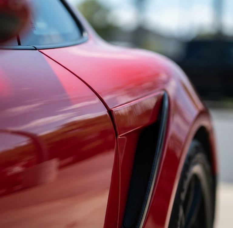Macro close-up of a high-end sports car fender, bright natural daylight highlighting deep glossy paint reflections and sharp metallic curves, shallow depth of field