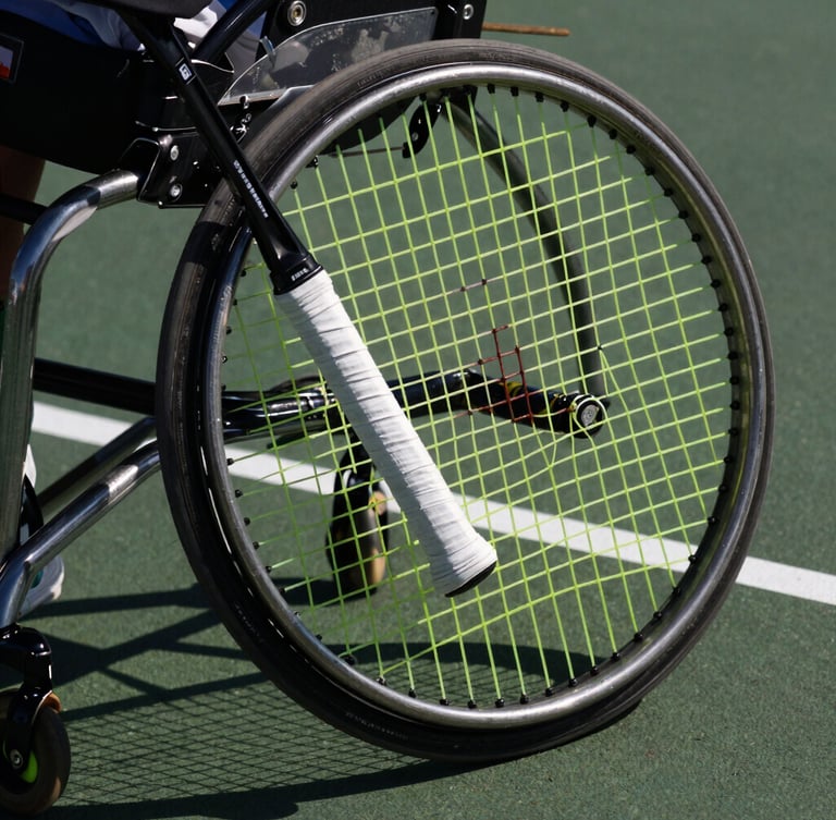 Macro crop of a tennis racket grip and a spinning wheelchair wheel on a dark hard court, intense direct sunlight casting strong shadows, 85mm.