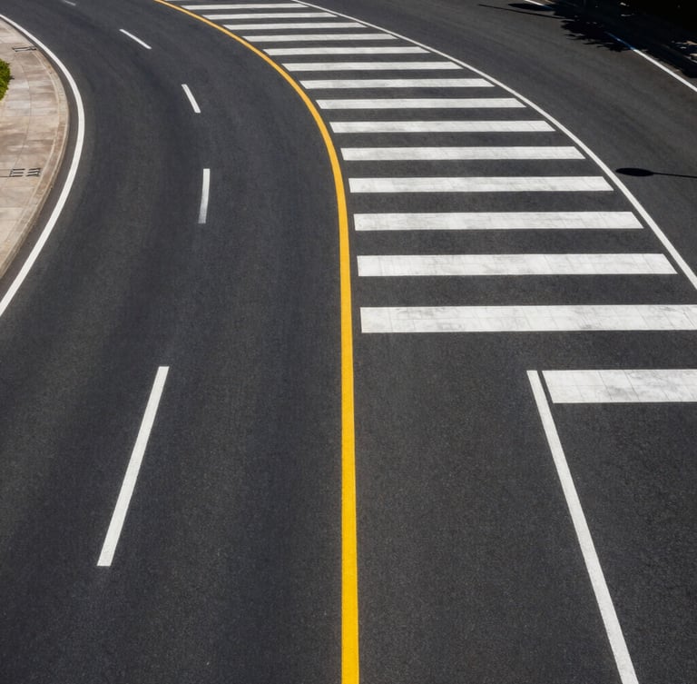 High-angle drone shot of a perfectly striped municipal highway curve under bright midday sun, pristine white and yellow thermoplastic lines stretching into the distance, deep black asphalt texture.