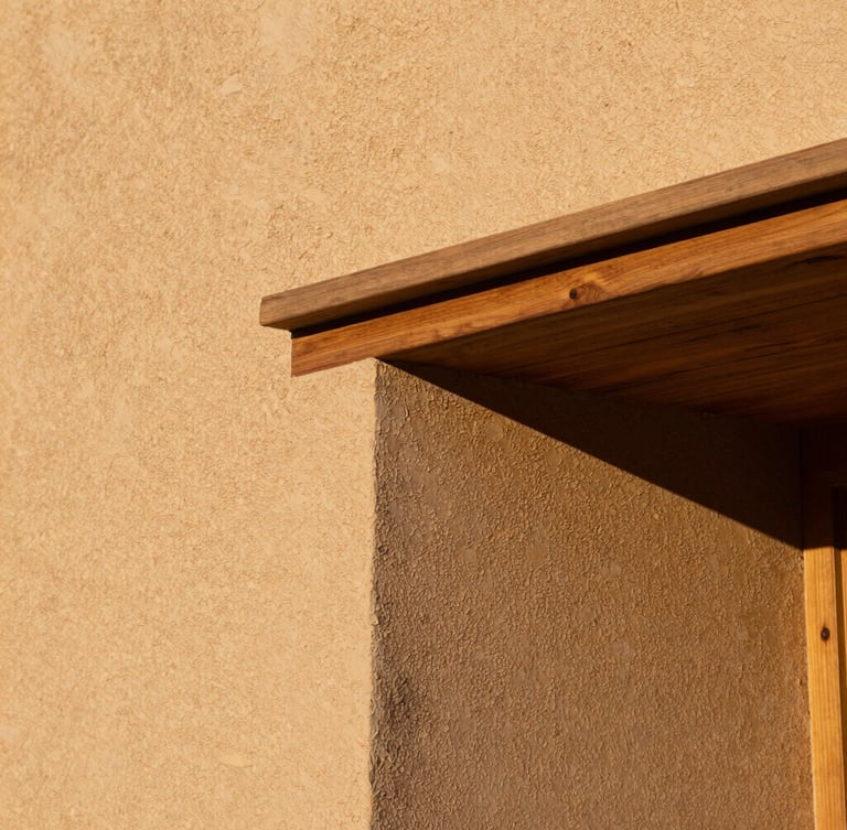 Close-up architectural detail of textured raw plaster walls meeting a heavy oak lintel, warm golden-hour side lighting, tactile textures, 35mm lens.