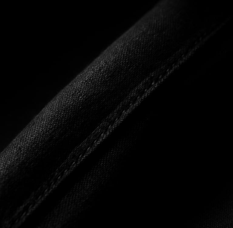 High-contrast studio photography of a heavy matte black fabric seam, deep chiaroscuro shadows, sharp key light highlighting the dense weave, 35mm.