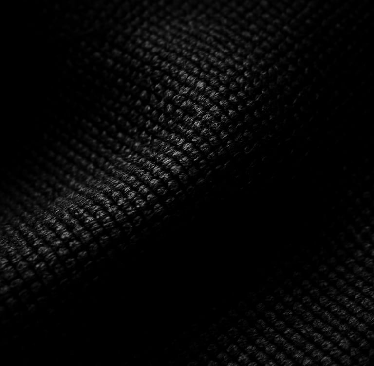 Tight macro crop of heavy black fabric texture, high-contrast chiaroscuro studio lighting, deep shadows, sharp key light highlighting dense weave, 35mm