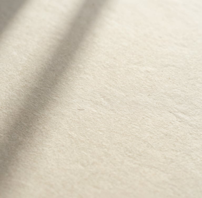 Extreme macro crop of debossed black ink on heavy cream paper stock, casting subtle shadows under soft window light.