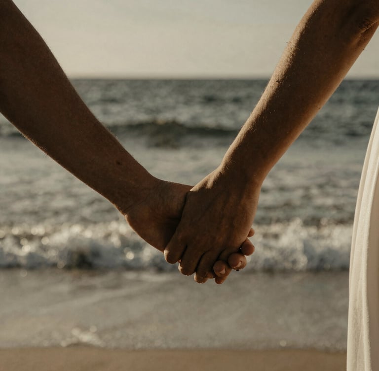 Close-up of a couple's hands gently intertwined, wind-blown ocean spray in the background, warm desaturated tones, dramatic natural light