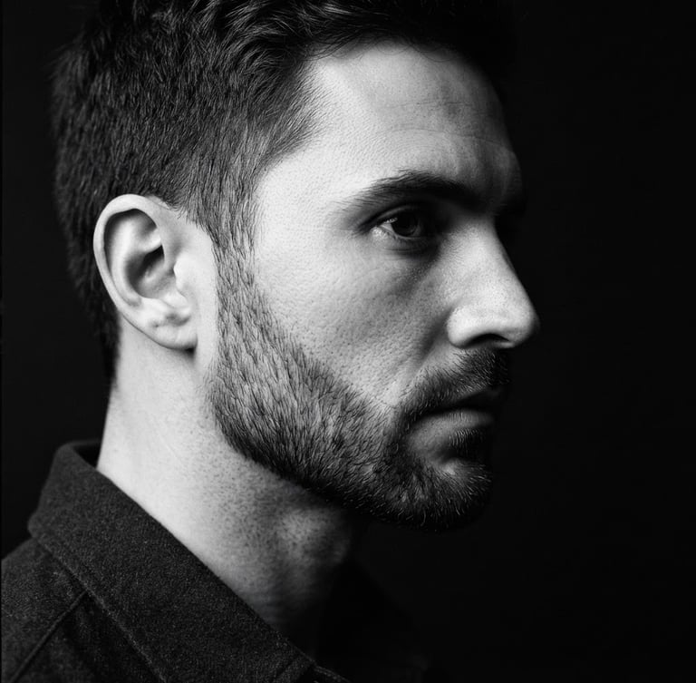 High-contrast black and white photography, close-up of a man's sharp jawline and perfectly groomed beard, dramatic side lighting, deep shadows, premium editorial style, 35mm lens