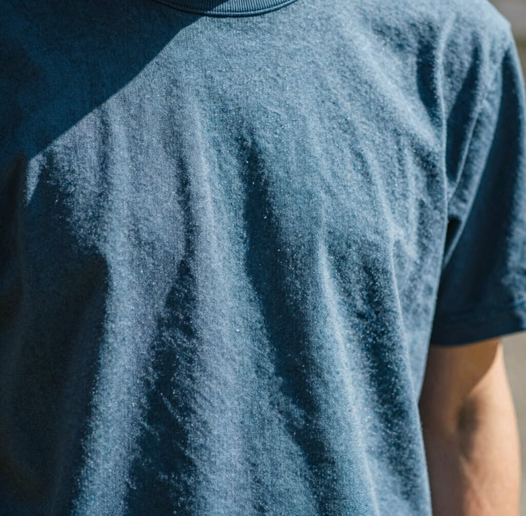 Close-up of thick textured cotton fabric of a blue t-shirt, sunbeams casting sharp linear shadows across the weave, warm minimalist aesthetic