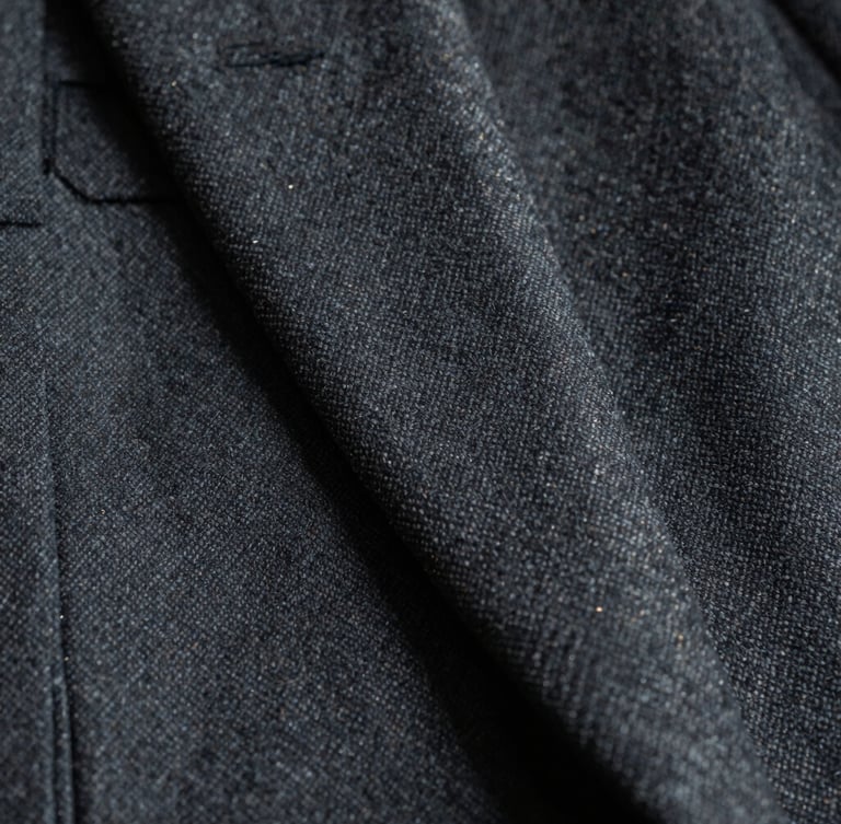 Severe cinematic macro shot of tailored dark grey wool suit fabric, sharp focus on the weave, deep shadows, cool daylight, gold thread detail