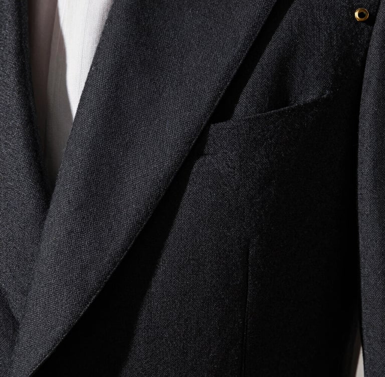 Extreme close-up of a dark tailored charcoal suit fabric, sharp focus on the weave, dramatic side lighting from a high window, deep shadows, gold cufflinks reflecting light.