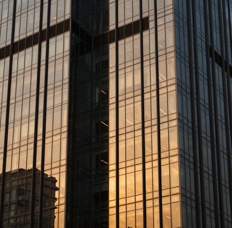 Architectural close-up of a modern corporate glass tower in Gurugram, dramatic golden hour light, deep charcoal shadows and warm gold reflections on the facade, sharp 35mm lens.
