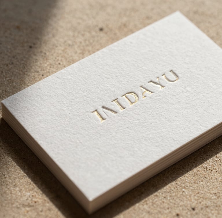 Macro shot of premium heavy-weight cotton business card with deep blind letterpress embossing and gold foil edge gilding, dramatic side lighting casting deep shadows on warm sand background.