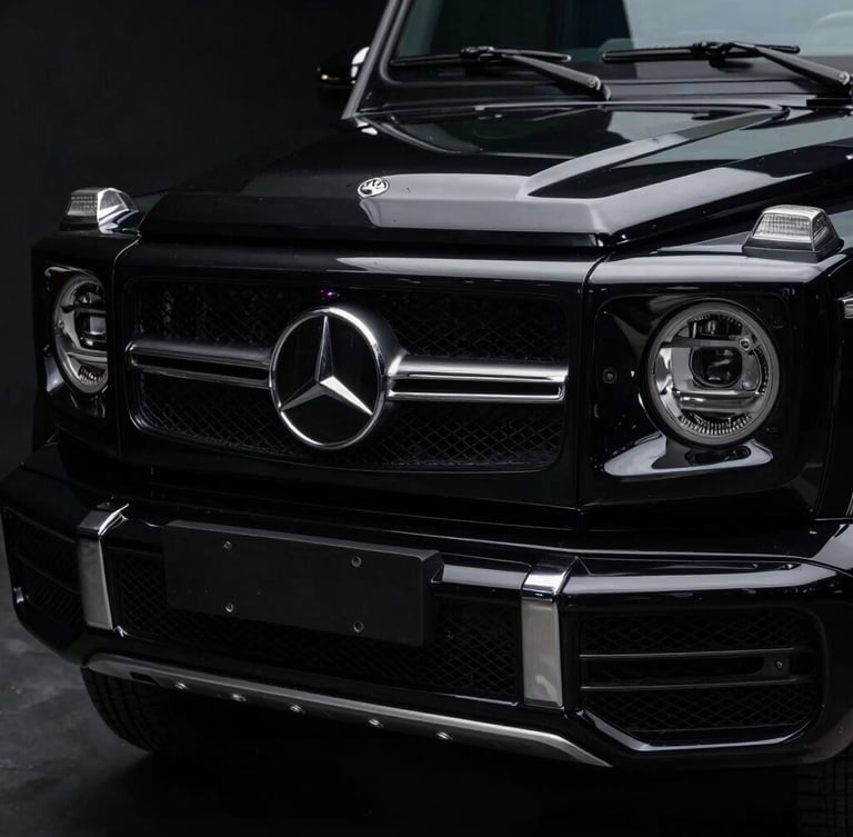 Low-key dramatic studio lighting on a black Mercedes G-Class grille, sharp metallic reflections, high contrast dark environment