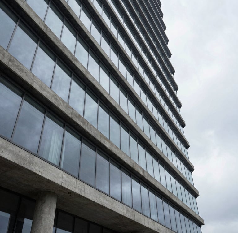 Wide architectural angle of a modern concrete and glass high-rise facade, clean geometric lines, diffused overcast daylight, reflecting a quiet sky.