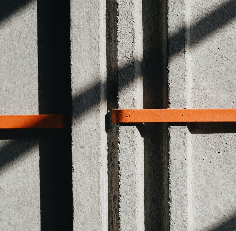 Extreme close-up of thick, textured cotton fabric seams against a rough concrete background, harsh architectural shadows, desaturated tones with a sharp orange accent.