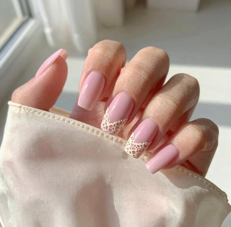 Macro shot of hand-painted pastel pink press-on nails with delicate cream lace details held against a vintage silk slip, soft morning sunlight, shallow depth of field