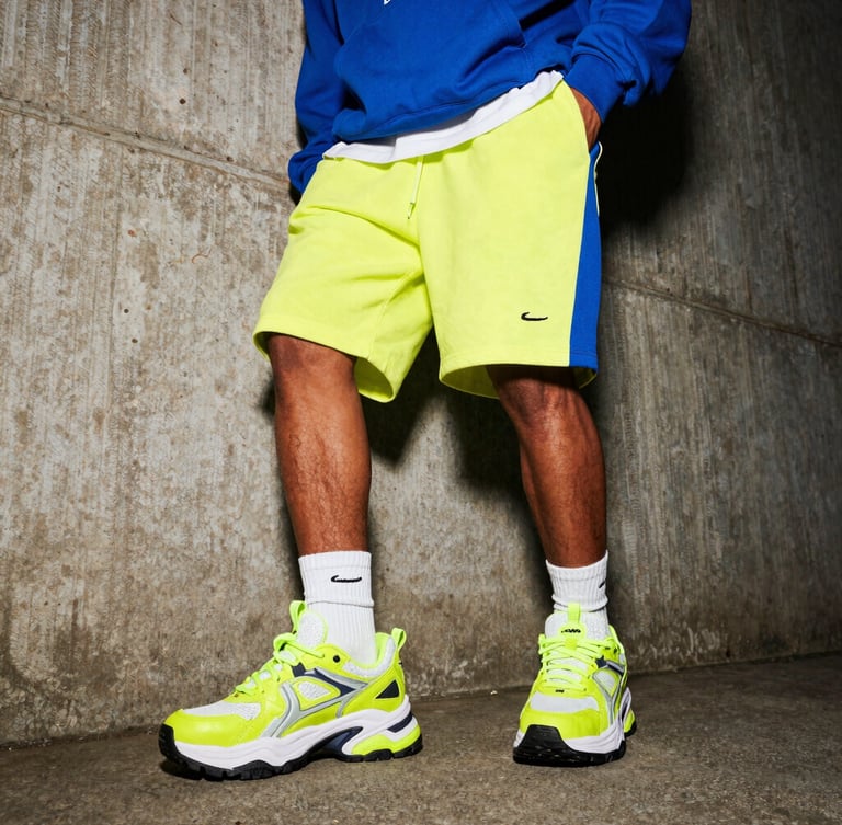 Dynamic low-angle shot of a model in Nairobi wearing chunky neon-accented sneakers and oversized streetwear hoodie, raw urban concrete background, high-contrast flash lighting