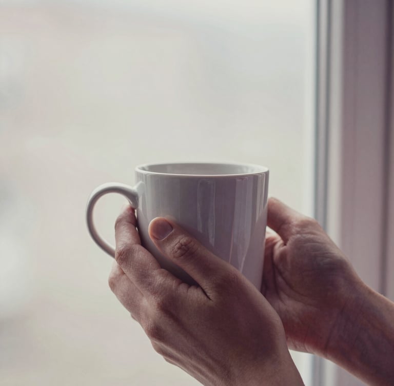 Close-up of hands holding a warm ceramic mug near a window, soft diffused morning light, muted pastel tones, shallow depth of field, 35mm