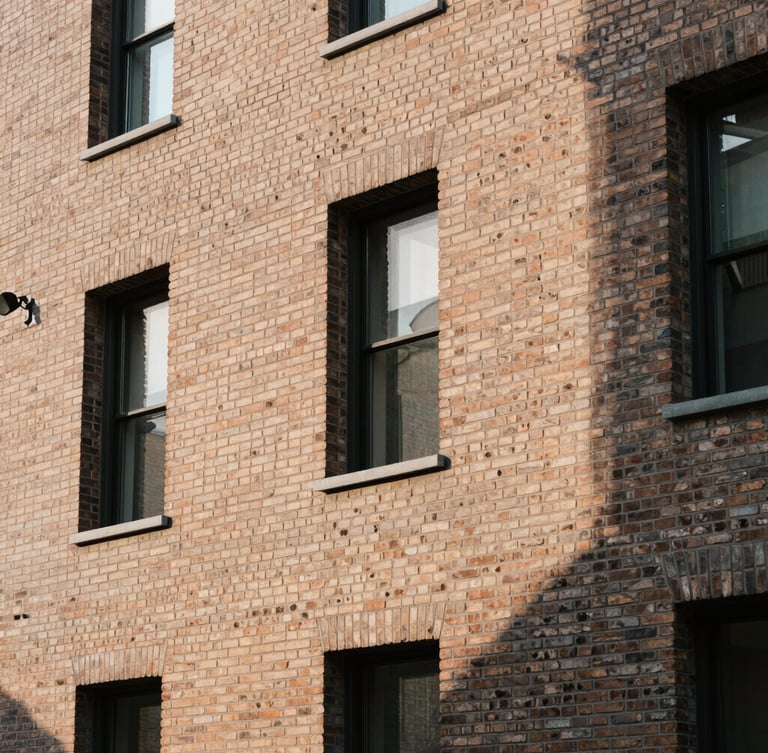 Warm editorial architectural photography of a modern brick facade, sharp geometric shadows, soft morning light, 35mm lens.