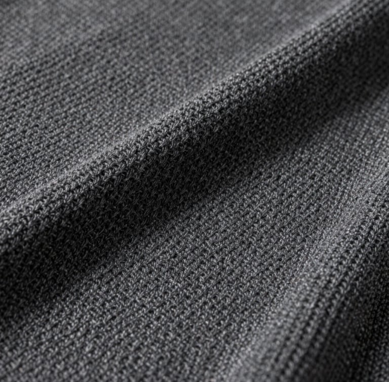 Studio close-up of a premium charcoal Reserva knit texture, showing clean geometric weave under soft neutral studio light.