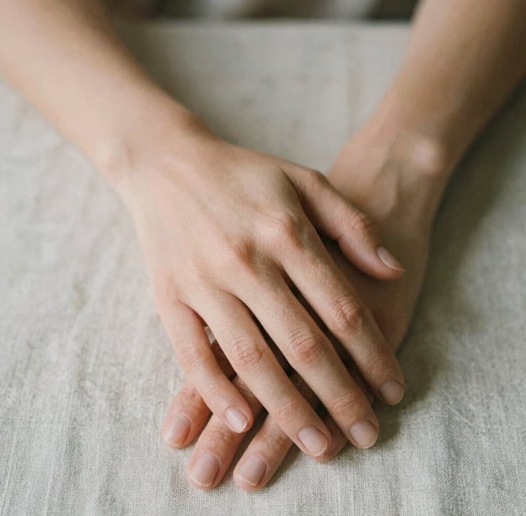 Close-up of hands gently resting on a textured linen cloth, soft diffused daylight, warm editorial photography, shallow depth of field