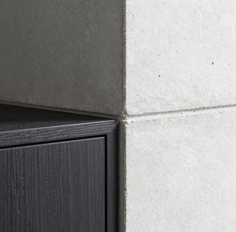 Close-up macro shot of a flawless architectural join, clean shadow-gap detailing between concrete wall and dark oak cabinet, natural side lighting, sharp shadows