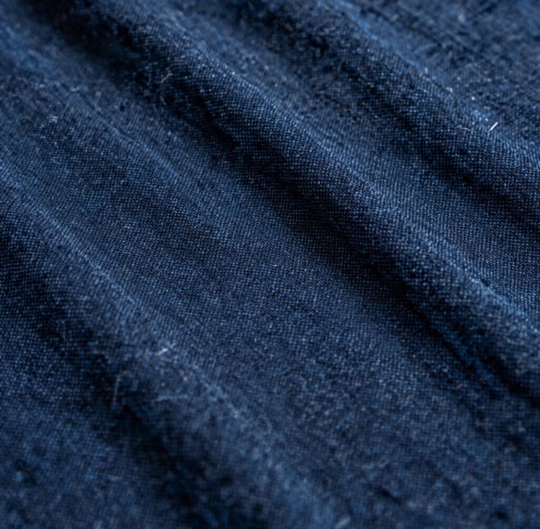 Macro texture of rich indigo dyed cotton fabric, warm natural side-light, showing intricate handloom weave details, 35mm photography