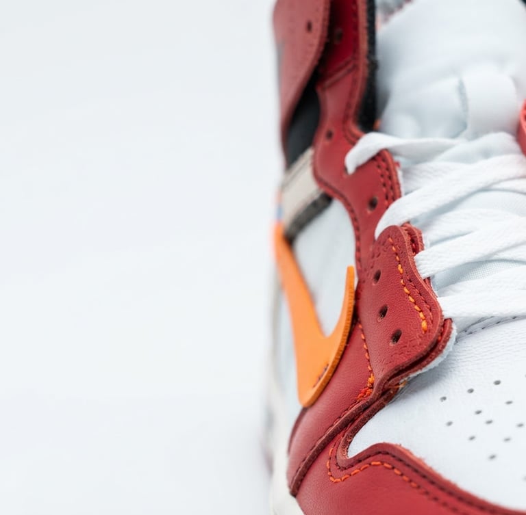 Tight macro shot of rare sneaker stitching, high-contrast studio lighting, clean white background, vibrant orange accents, 50mm lens, right third.