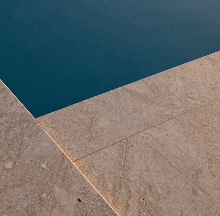 Close-up of premium warm travertine pool coping meeting deep blue water, textured natural stone, soft twilight lighting, architectural photography