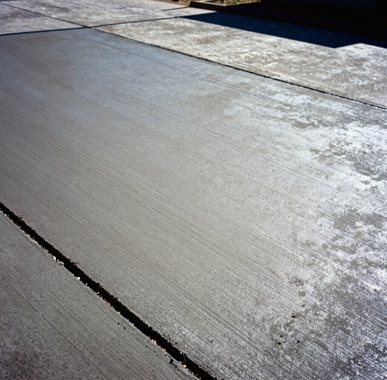Low-angle heroic shot of freshly poured concrete driveway in Birmingham, Alabama, high-contrast midday sun highlighting the smooth hand-troweled texture, deep shadows, 35mm.
