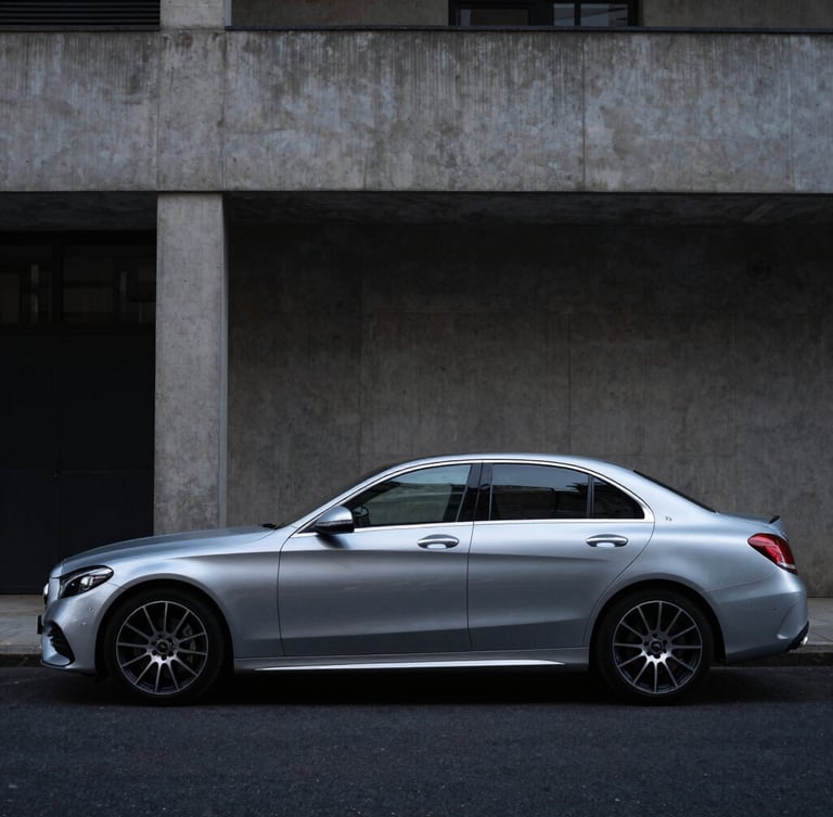 Wide-angle profile shot of a clean metallic silver Mercedes C-Class parked against a minimalist concrete architectural facade in South London, moody overcast daylight, 35mm lens